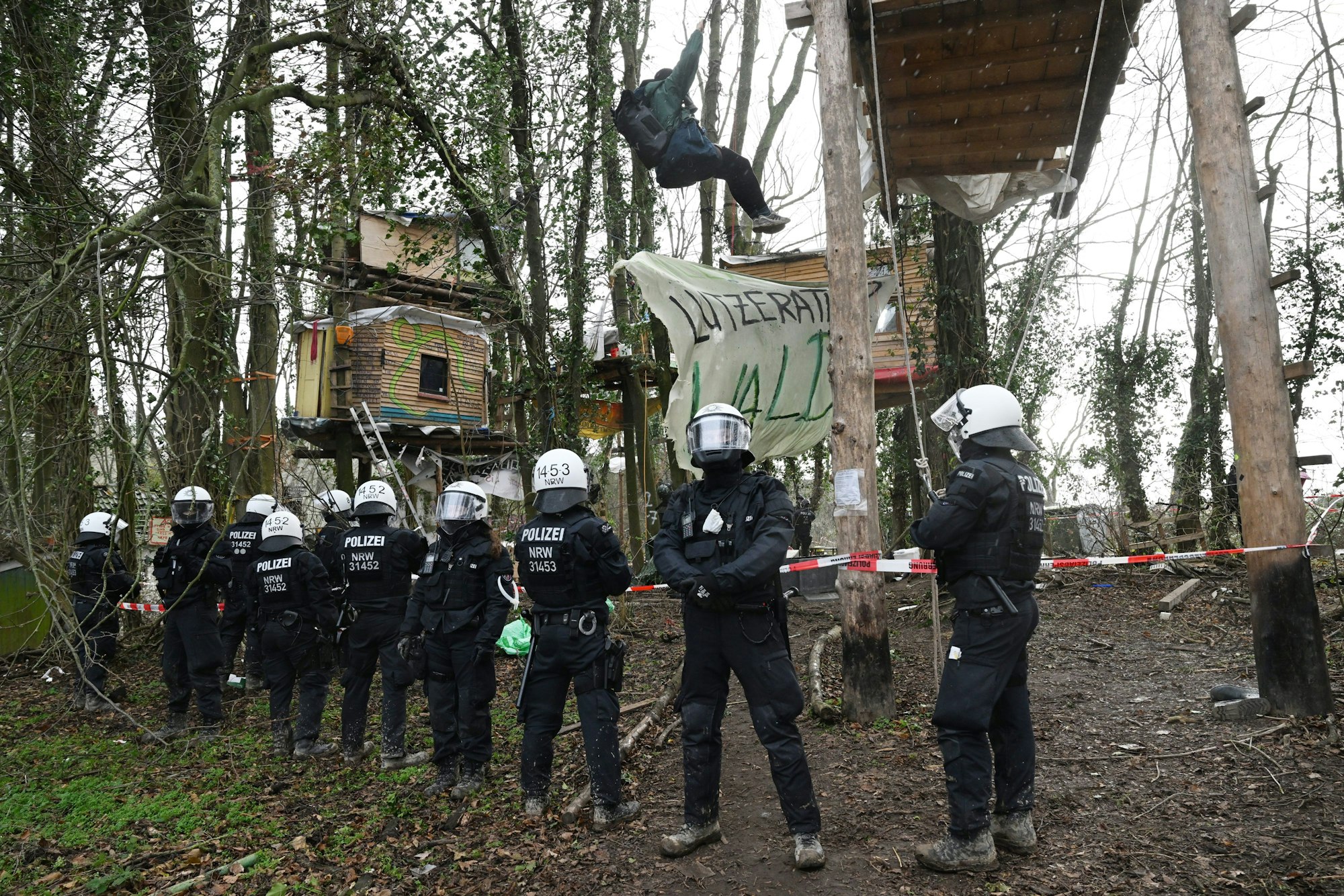 Polizisten stehen am dritten Tag der Räumung im von Klimaaktivisten besetzten Braunkohleort Lützerath vor Baumhütten der Aktivisten.