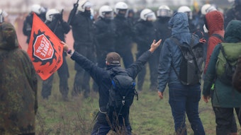Ein Demonstrant geht vor Polizisten bei der Demonstration von Klimaaktivisten am Rande des Braunkohletagebaus bei Lützerath mit ausgebreiteten Armen auf die Knie.
