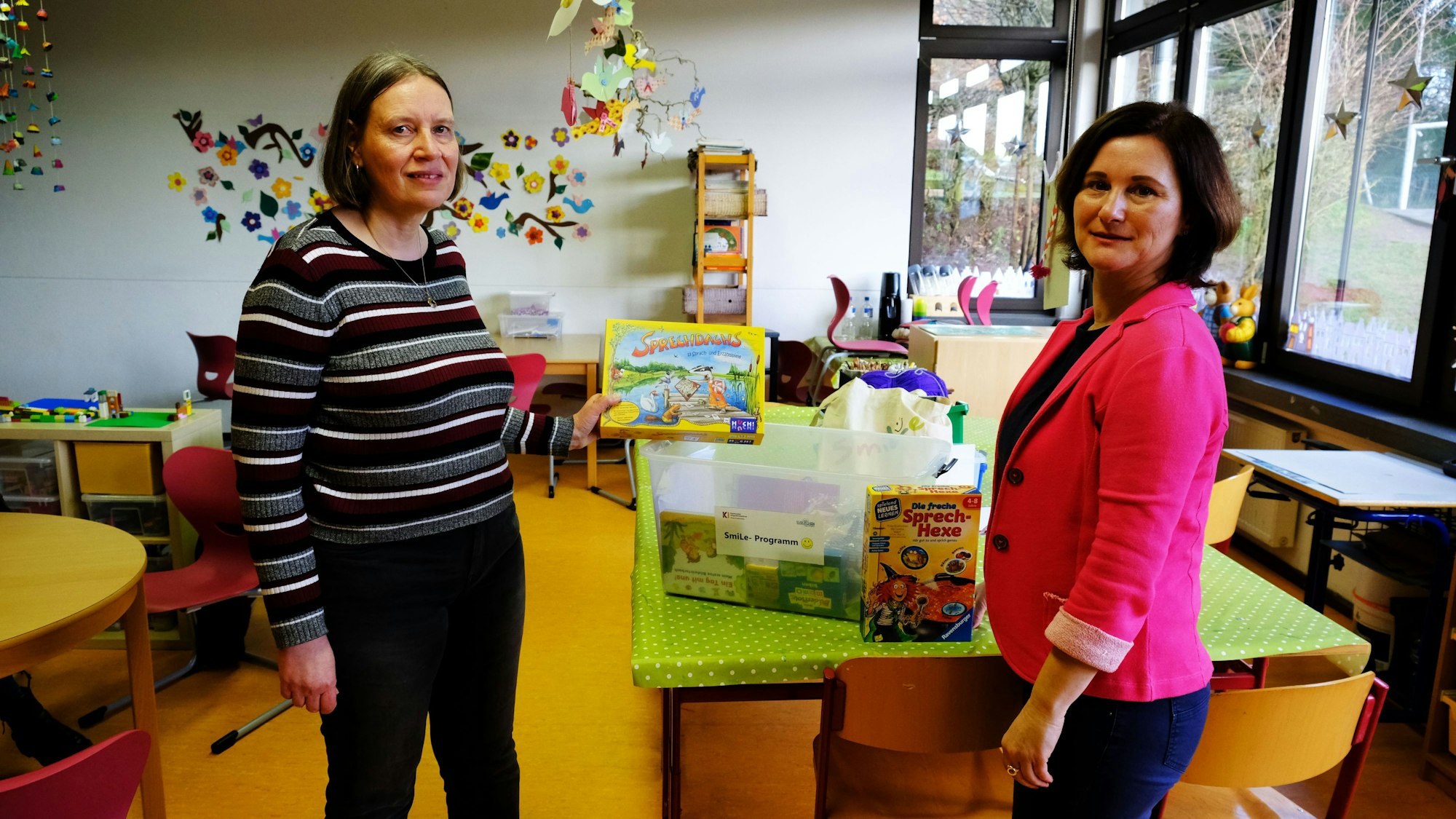 Koordinatorin Suzana Kilickeser und Sprachpatin Ulrike Schmitz präsentieren auf einem Tisch in einem Klassenzimmer der Grundschule Reifferscheid Spiele und Spielsachen.