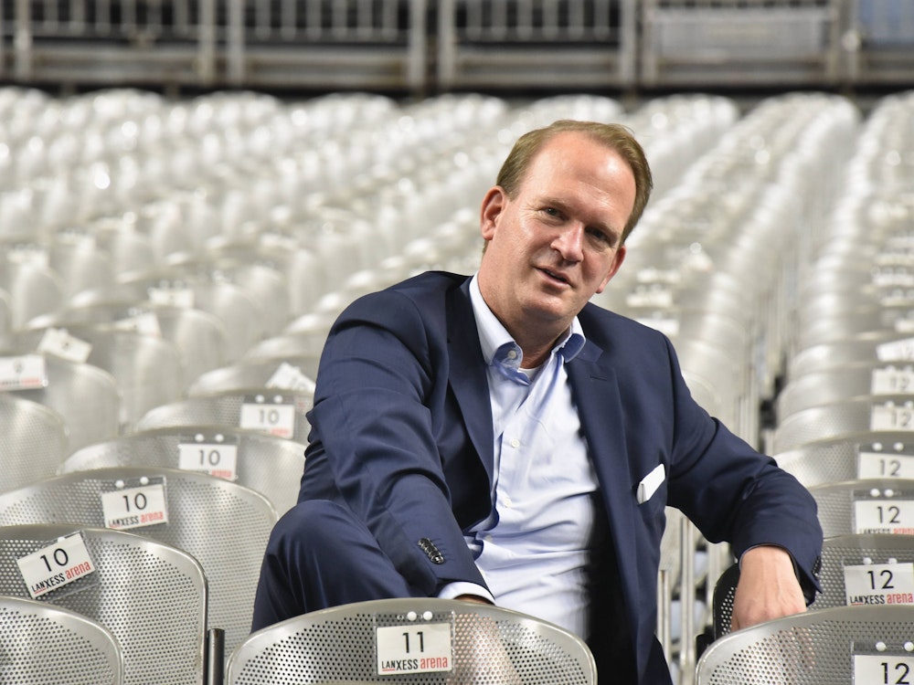 Stefan Löcher, Geschäftsführer der Lanxess-Arena sitzt in einer Stuhlreihe der leeren Lanxess-Arena.