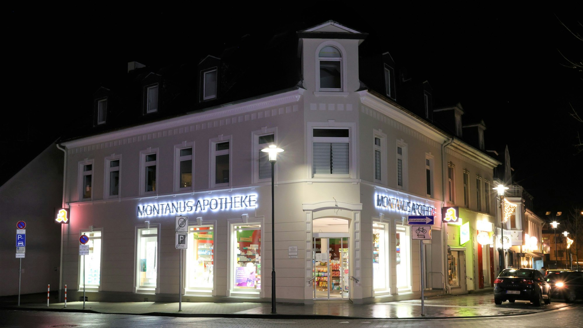 Ein Altbau-Eckhaus bei Nacht, im Erdgeschoss befindet sich die beleuchtete Montanus-Apotheke.