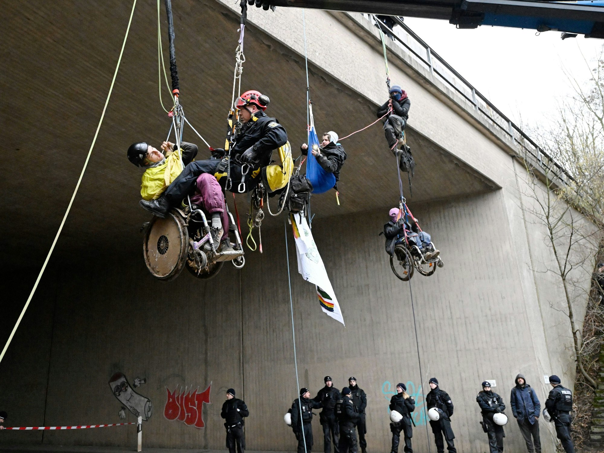 Ein Höhenretter der Polizei hilft einem  Umweltaktivisten im Rollstuhl auf den Boden.