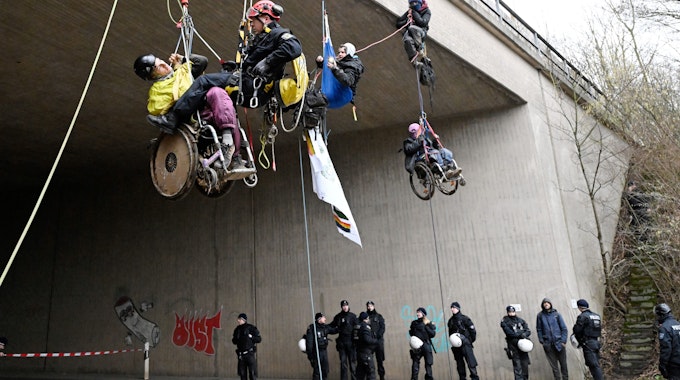 Ein Höhenretter der Polizei hilft einem  Umweltaktivisten im Rollstuhl auf den Boden.