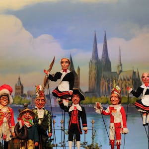 Stockpuppen des Hänneschentheaters vor dem Kölner Rheinpanorama: Rote Funken und Hellige Knäächte un Mägde posieren mit Speimanes und Sitzungsleiter Schäng.