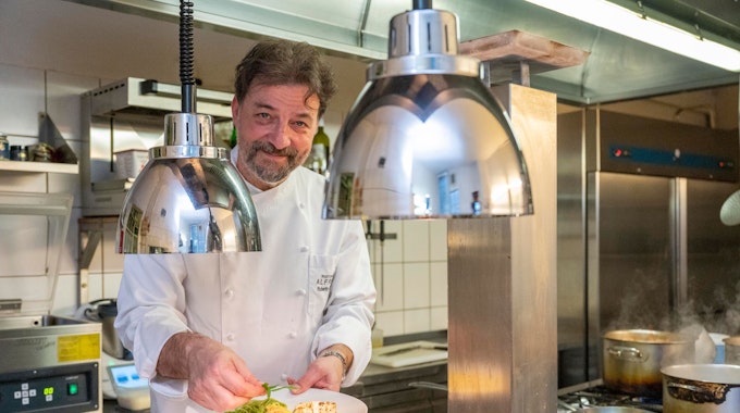 Roberto Carturan steht in&nbsp;&nbsp;Kochkleidung in seiner Küche und hält einen Teller mit Essen in der Hand