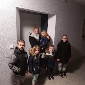 Eine Frau steht mit ihren Kindern vor einer Tür.