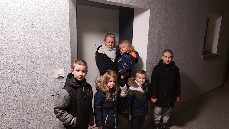 Eine Frau steht mit ihren Kindern vor einer Tür.