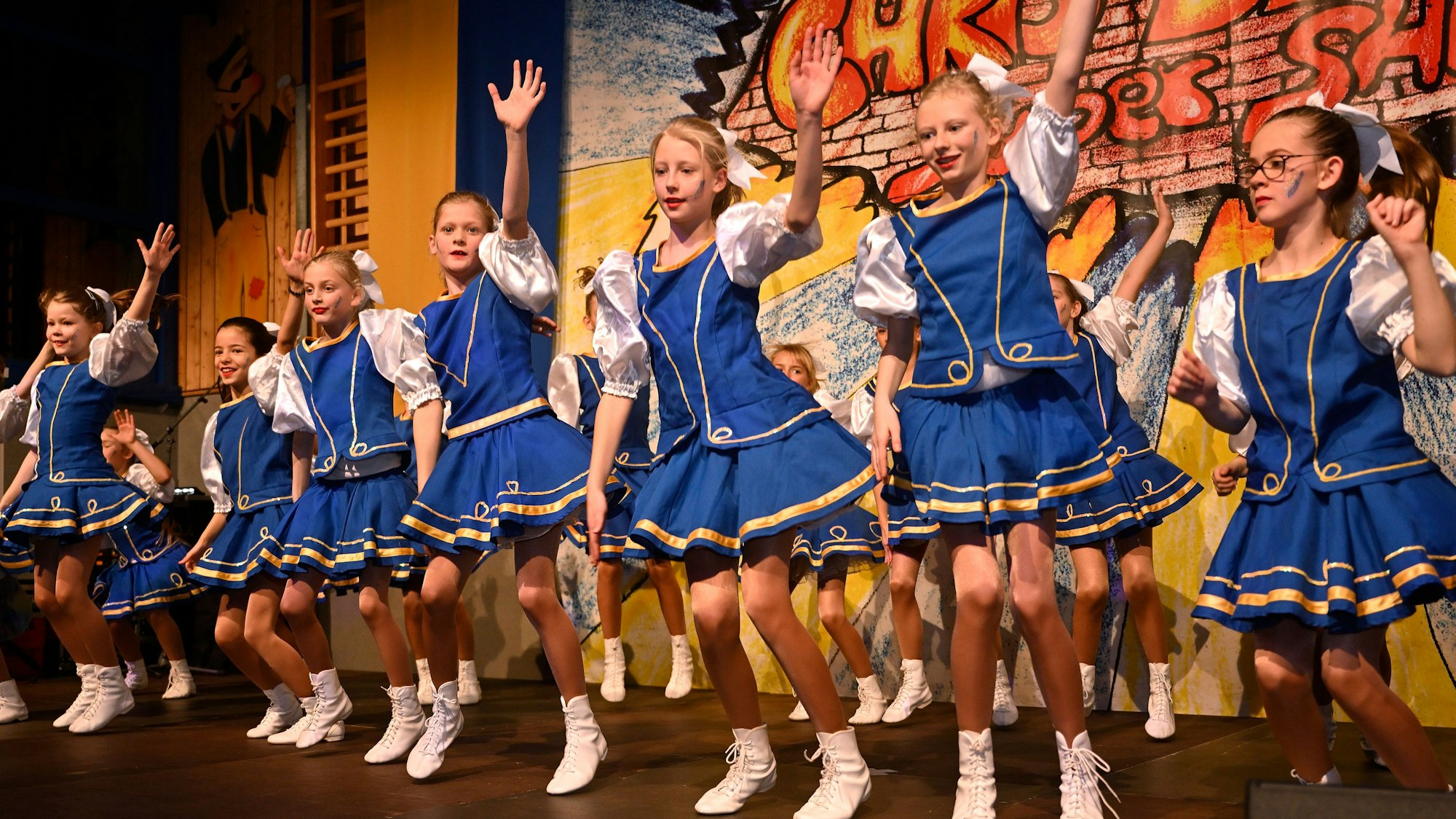 Die 20-köpfige Kindertanzgruppe Chri-Di-Ro-Gos Pänz tanzt in blauen Kleidern auf der Bühne.