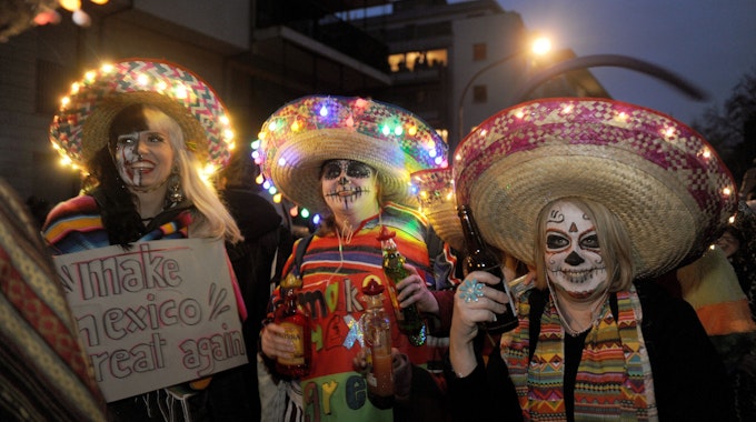 Drei als Geister geschminkte Menschen mit Sombreros mit Lichterketten.