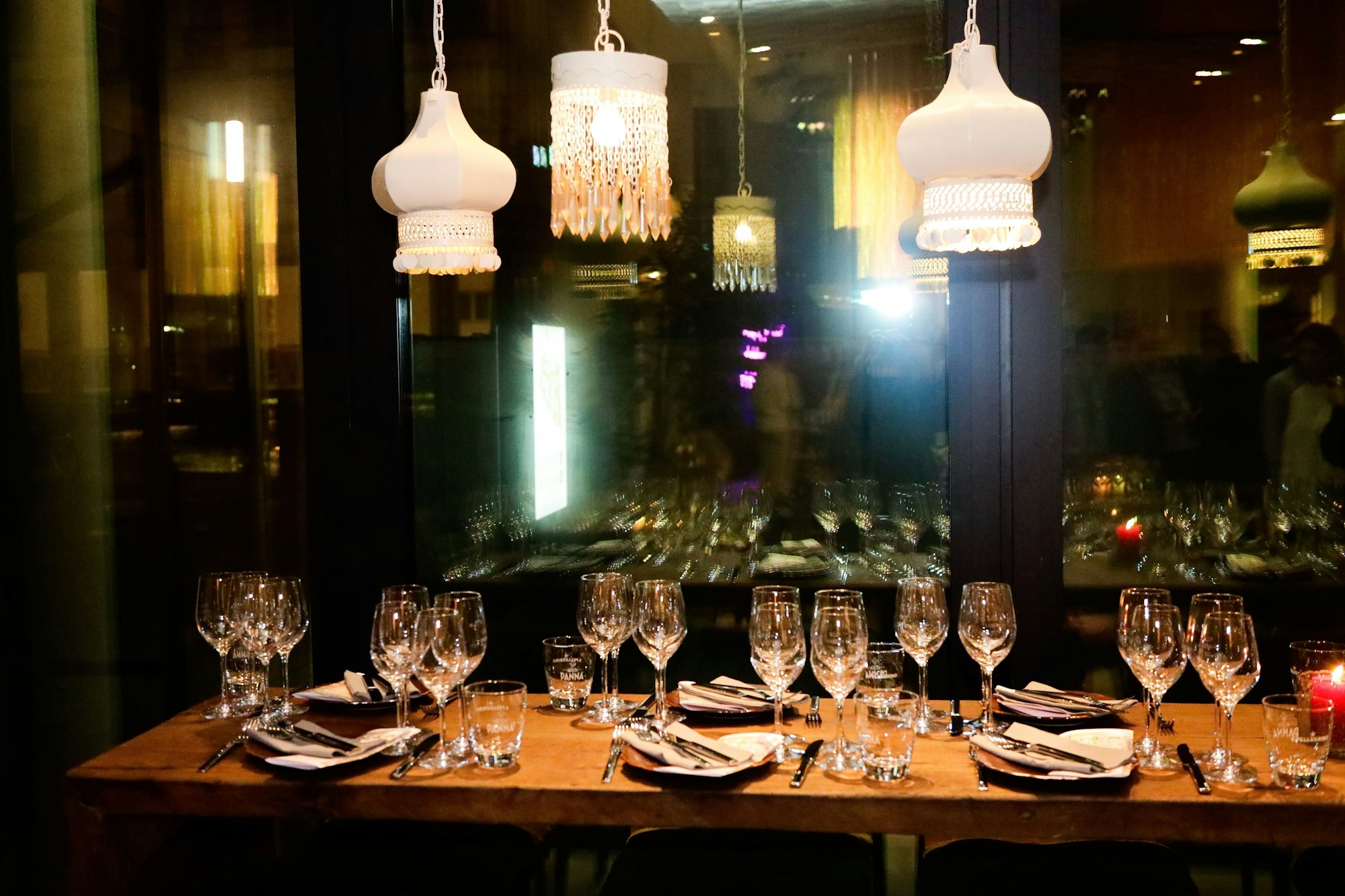 Ein gedeckter Tisch vor dunklen Fensterscheiben, von der Decke hängen Lampen mit orientalischen Stoffschirmen.