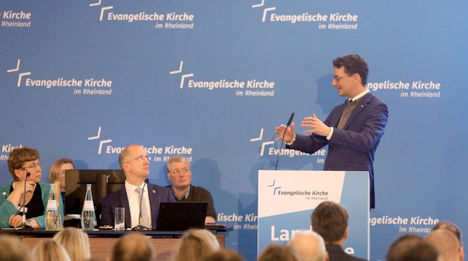 Der nordrhein-westfälische Ministerpräsident Hendrik Wüst (CDU) spricht während der Landessynode der Evangelischen Kirche im Rheinland zu den Teilnehmern, links sitzt Thorsten Latzel, Präses der Evangelischen Kirche im Rheinland.