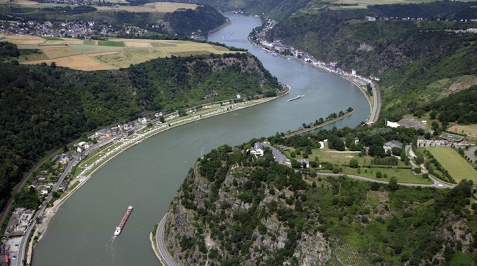 Der Rhein schlängelt sich durch die grüne Landschaft des Mittelrheintals beim Loreley-Felsen. Frachschiffte fahren auf dem Fluss.