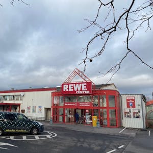 Vor dem Rewe-Center in Brühl-Ost parken Autos, ein Kunde schiebt seinen Einkaufswagen ins Geschäft.