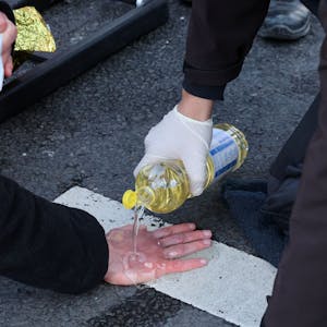 Ein Beamter der Polizei schüttet Speiseöl über die Hand einer Aktivistin.