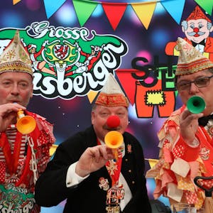 Rainer Furth-Quernheim (Große Bensberger), Harald Hahn (Förderverein Refrather Karneval) und Schlader-Botze-Chef Michael „Mio“ Oppermann (v.l.) stehen in Karnevalsklamotten mit bunten Tröten vor buntem Hintergrund.