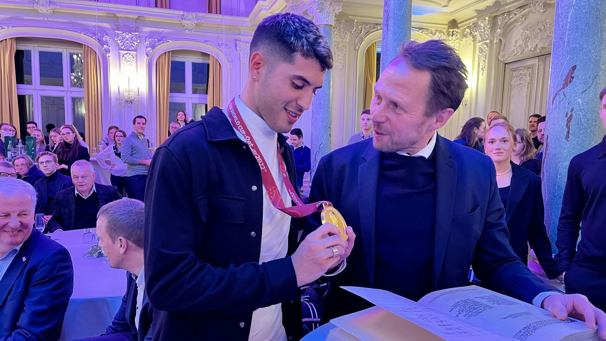 Exequiel Palacios zeigt Uwe Richrath seine goldene WM-Medaille