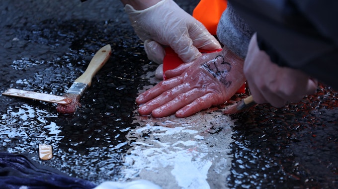 Die angeklebten Hände einer Demonstrantin werden mit Speiseöl vom Asphalt gelöst.
