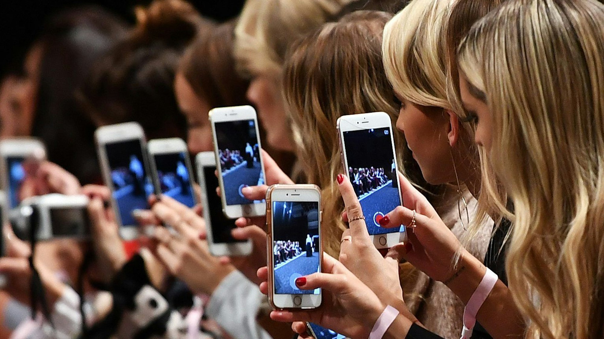 Frauen mit Smartphones filmen und fotografieren eine Modenschau.