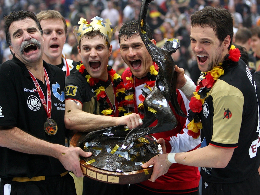 Trainer Heiner Brand (l-r) hält den WM-Pokal zusammen mit seinen Spielern Michael Kraus, Torwart Henning Fritz und Kapitän Markus Bauer.