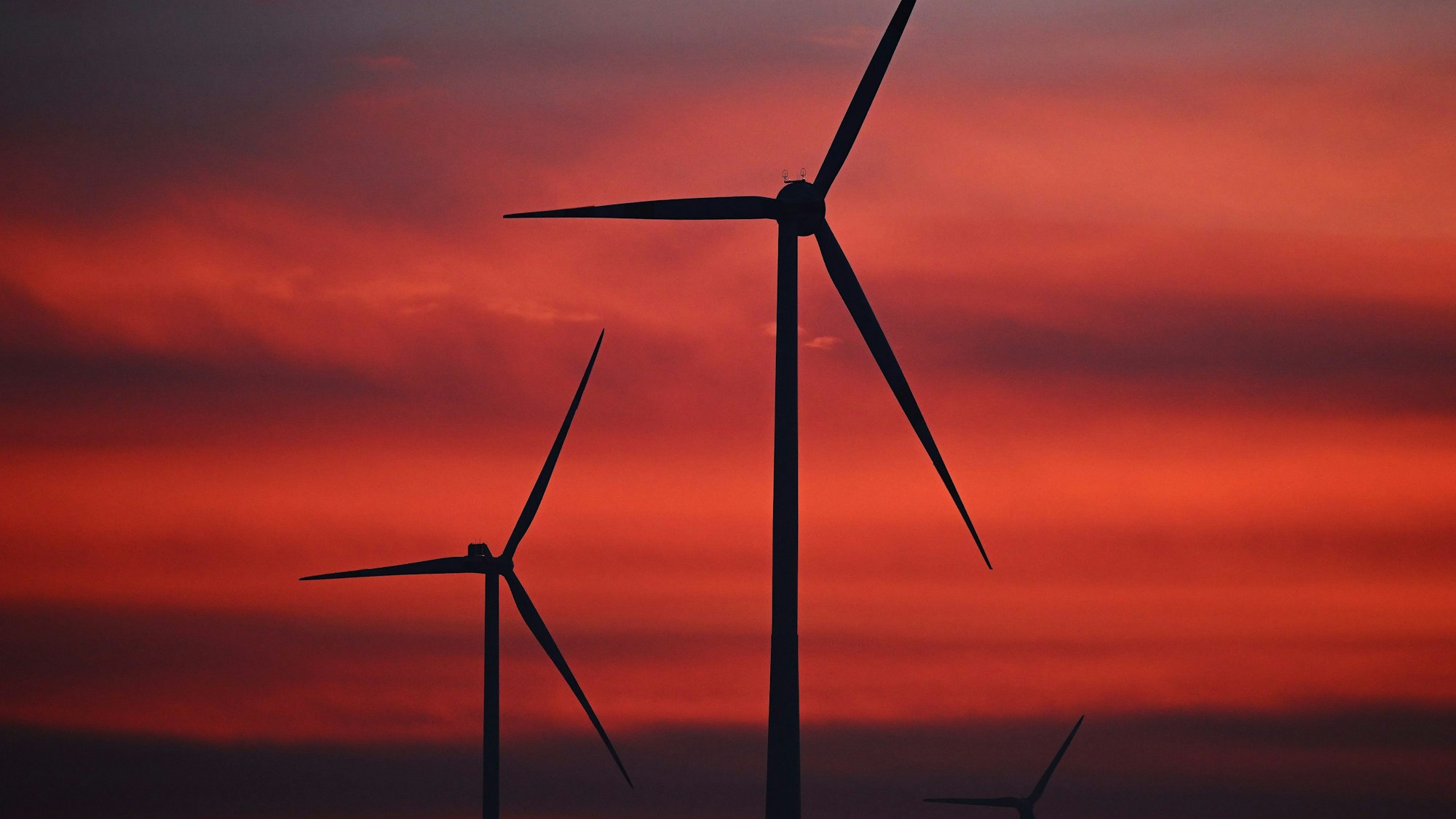 Diese Windräder in einem Windpark wurden bei Sonnenaufgang fotografiert. Diese Aufnahme ist ein Symbolfoto.
