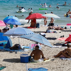 Symbolfoto: Menschen liegen am Strand von Cala Major, in der Nähe von Palma auf Mallorca, oder halten sich im Wasser auf.