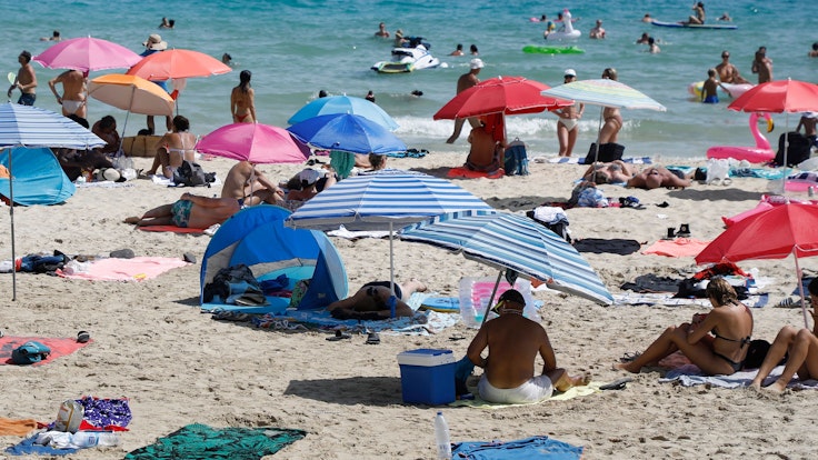 Symbolfoto: Menschen liegen am Strand von Cala Major, in der Nähe von Palma auf Mallorca, oder halten sich im Wasser auf.