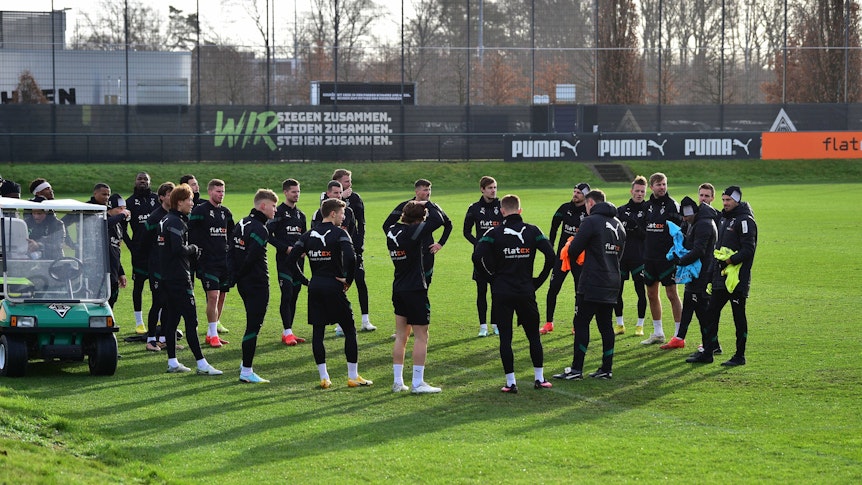 Die Spieler von Borussia Mönchengladbach und einige Mitglieder des Trainerstabs stehen im Rahmen einer Trainingseinheit auf dem Trainingsplatz im Borussia-Park im Kreis. Alle Spieler tragen dabei dunkle Borussia-Trainingskleidung, aufgenommen wurde das Foto am 10. Januar 2023.