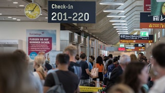 Zahlreiche Passagiere warten am Flughafen Köln/Bonn an der Sicherheitskontrolle. Es ist ein Schild mit Hinweisen zum Check-in zu sehen.