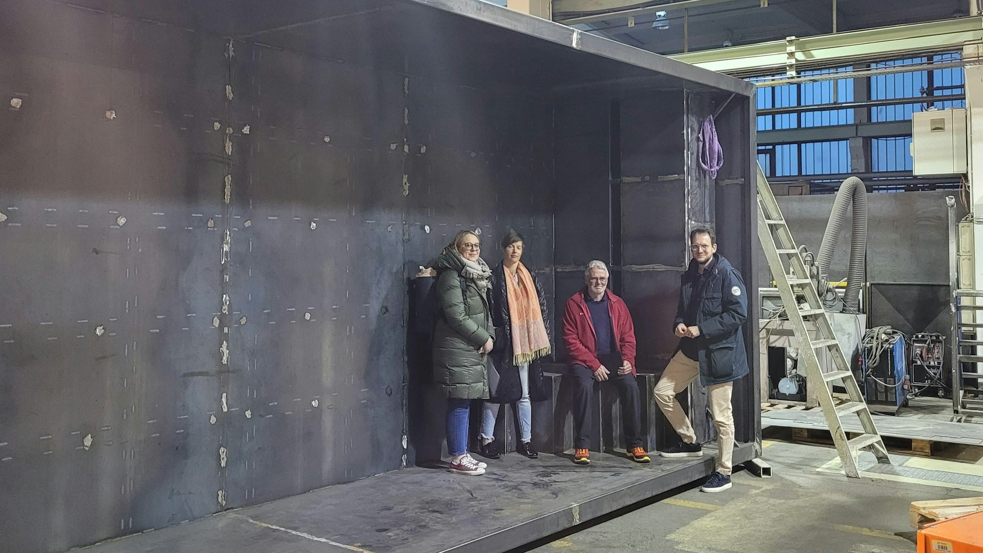 Vier Personen stehen und sitzen in einer dunklen Betonwanne, die auf der Seite liegt.