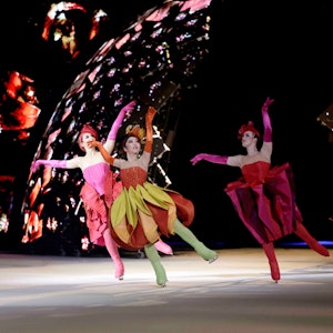 Eiskunstläufer der Show in farbenfrohen Kleidern. Im Hintergrund Farb- und Lichteffekte.