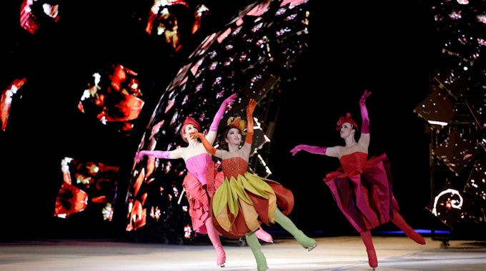 Eiskunstläufer der Show in farbenfrohen Kleidern. Im Hintergrund Farb- und Lichteffekte.