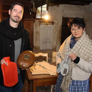 Ein Mann und eine Frau zeigen Hausmittelchen gegen die Kälte: Wärmflaschen, kupferne Bettwärmer und in Sohlenform geschnittenes Zeitungspapier.