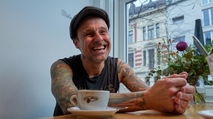 Ingo Knollmann lachend am Tisch im Café. Vor ihm steht eine Tasse Kaffee.