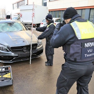 Eine Polizistin hält einen Maßstab an den sichergestellten Mercedes, ihr Kollege macht Fotos.
