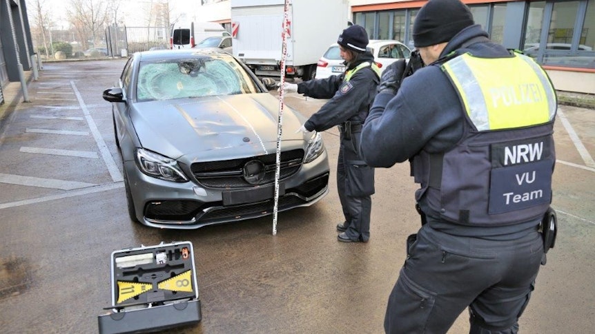 Eine Beamtin hält einen Maßstab an die Front des beschädigten Unfall-Mercedes, ihr Kollege macht Fotos.