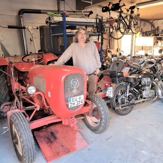 Ralf Meier aus Dottel steht in einer Garage neben einem roten Traktor und einem Motorrad.