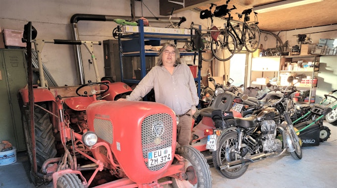 Ein Mann steht an einem alten Traktor, im Hintergrund sind einige Motorräder zu sehen.