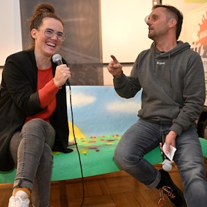 Katja Diehl sitzt neben Moderator Johannes Thies und lacht.