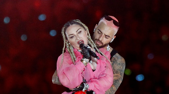 Madonna bei einem Live-Auftritt mit Sänger Maluma hinter ihr. Sie singt in ein Mikro.