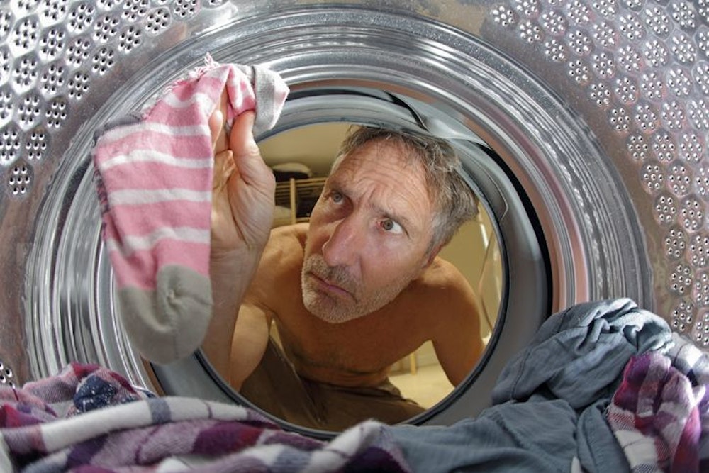 Mann schaut in Waschmaschine nach verlorenen Socken