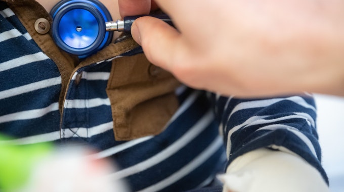 Ein Kinderarzt untersucht ein Kleinkind mit einem Stethoskop und hört ihm die Brust ab.