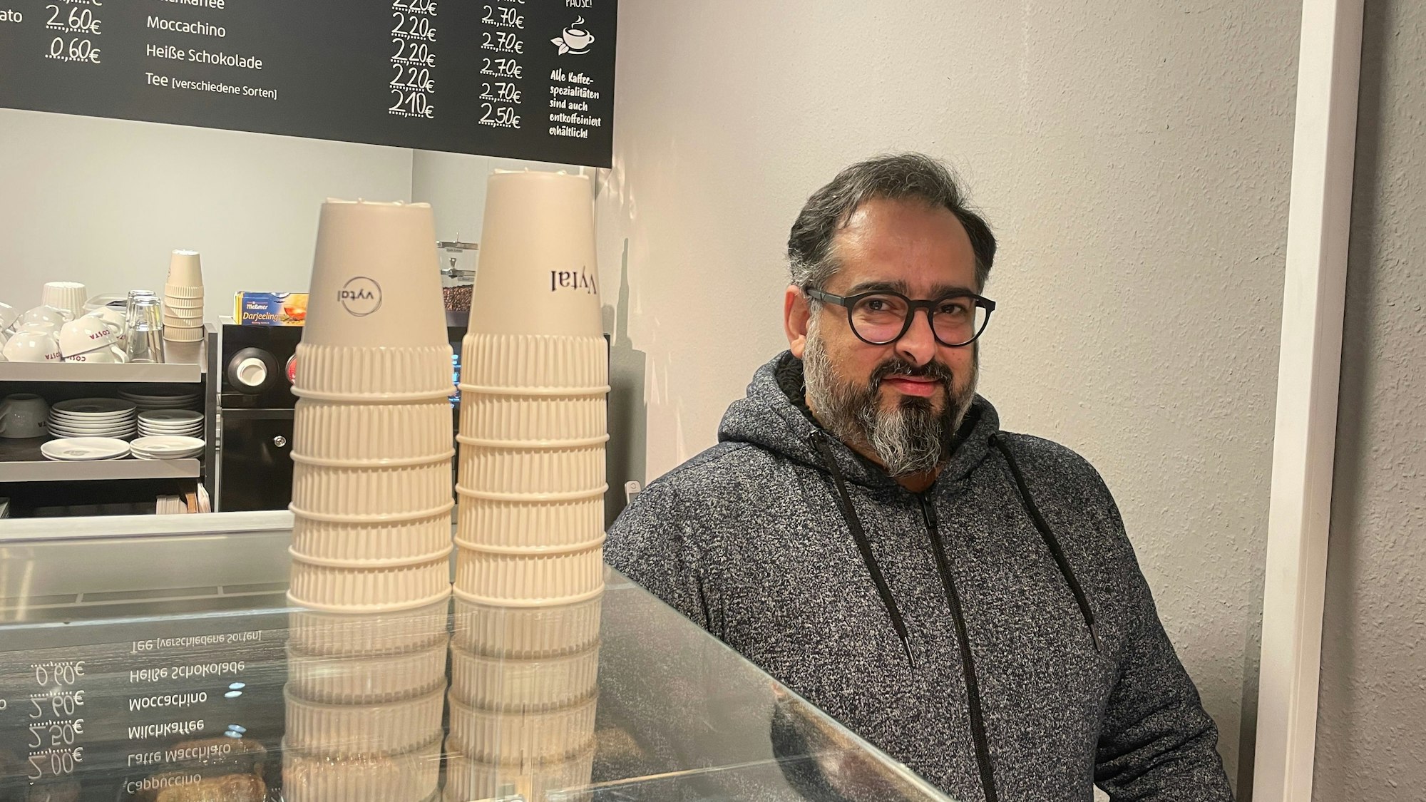Der Besitzer von Back Löwe, Farshid Sowlati, steht hinter der Theke. Neben ihm stehen Mehrwegbecher der Kölner Firma Vytal. Seit dem 1.1.2023 müssen Gastronomen Mehrwegbehälter zum Mitnehmen anbieten, die nicht teuerer sein dürfen als Einwegverpackungen.