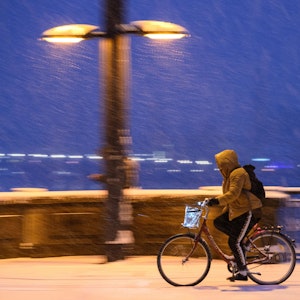 Eine Radfahrerin fährt am Morgen bei Schneefall.