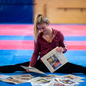 Kampfsportlerin Jessica Rau sitzt in ihrer Trainingshalle auf dem Boden und betrachtet Zeitungsartikel.