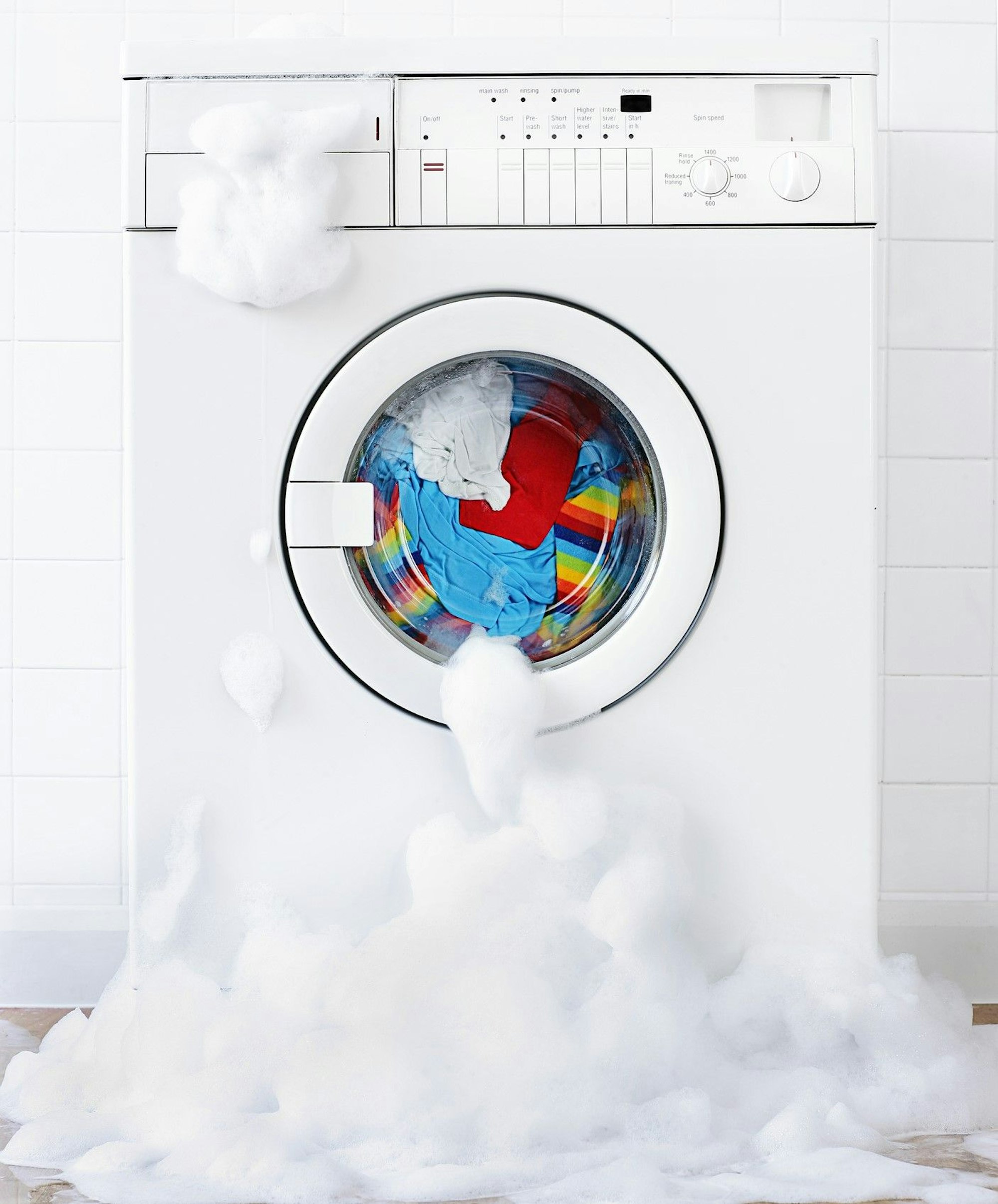 Waschmaschine, gefüllt mit bunter Wäsche, aus der Schaum ausläuft.