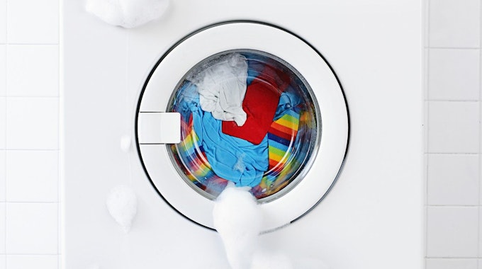 Waschmaschine, gefüllt mit bunter Wäsche, aus der Schaum ausläuft.