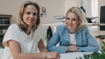 Die beiden Gründerinnen von Badesofa Natalie Steger (links) und Annika Götz sitzen an einem Besprechungstisch.