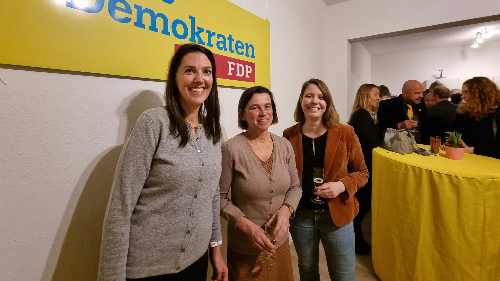 Drei Frauen stehen mit einem Glas Sekt in der Hand vor einem Banner mit der Aufschrift "Freie Demokraten - FDP" und lächeln in die Kamera.