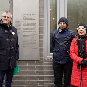 Andreas Wolter, Daniel Poštrak und Edith Lunnebach stehen vor der Gedenktafel zur Erinnerung an den NSU-Sprengstoffanschlag vom 19. Januar 2001 in Köln-Mülheim.