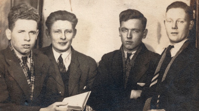 Auf einem alten Schwarz-Weiß-Foto stehen vier junge Männer in Anzug nebeneinander.